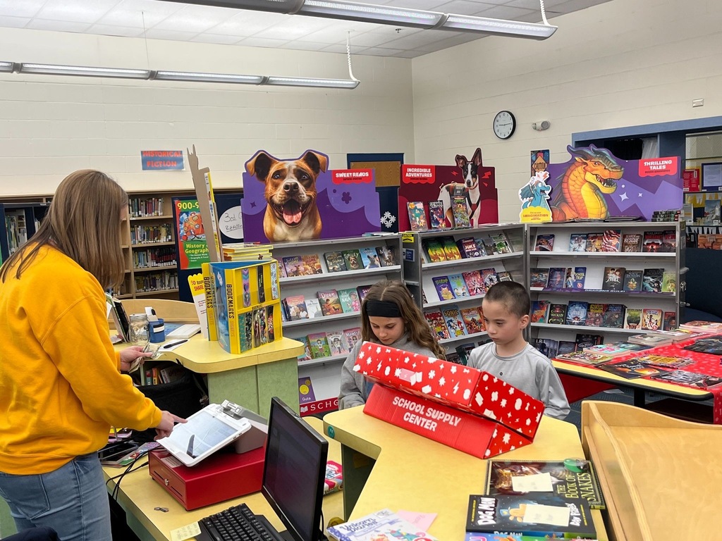 Students purchasing books at book fair. You can see shelves full of books in the background.