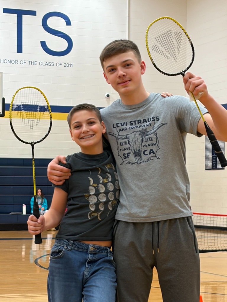 Two students standing side by side holding their badminton rackets in the gym.