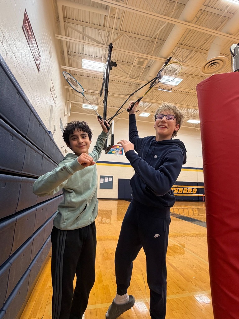 Two students standing side by side holding their badminton rackets in the gym.