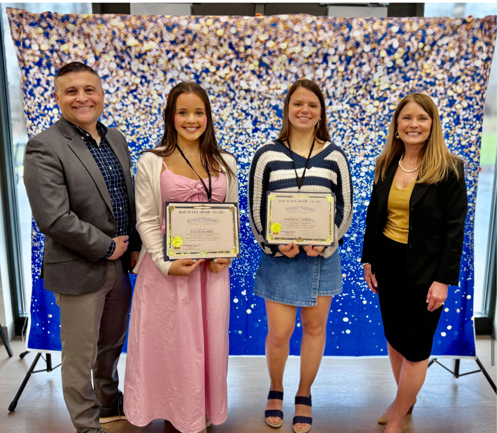 Two students holding awards with adults on either side of them. There is a photo backdrop behind them.