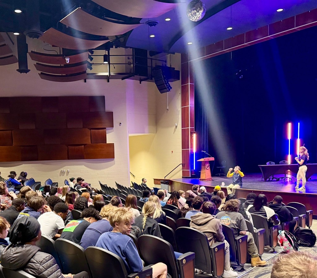 Students sit in the Streetsboro High School auditorium while there are two people on the stage during an assembly. 