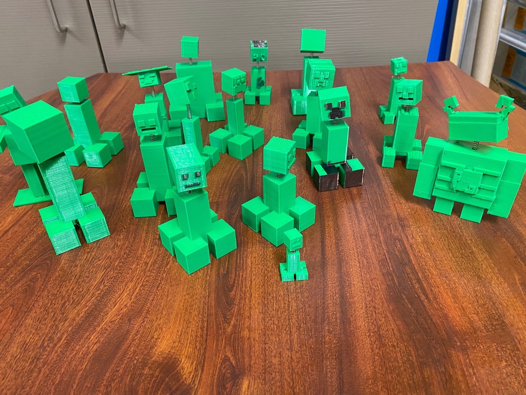 A collection of green 3D-printed Minecraft character bobblehead models displayed on a wooden desk.