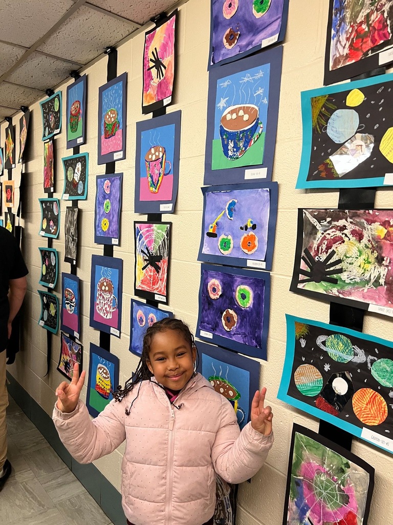  child stands in a hallway lined with colorful student artwork displayed on both walls, including space-themed paintings.