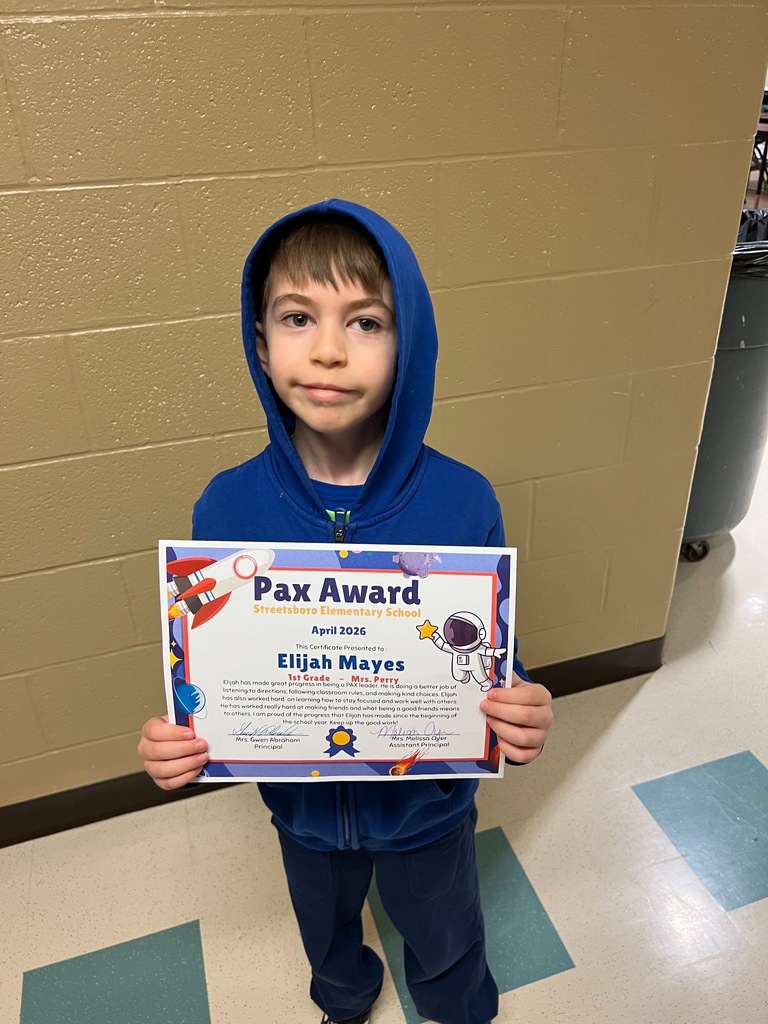 a student stands in front of a wall holding a certificate that says Pax Award