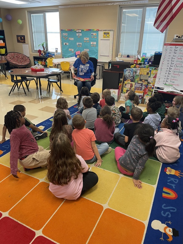 Students sitting on rug listening to an adult read them a story