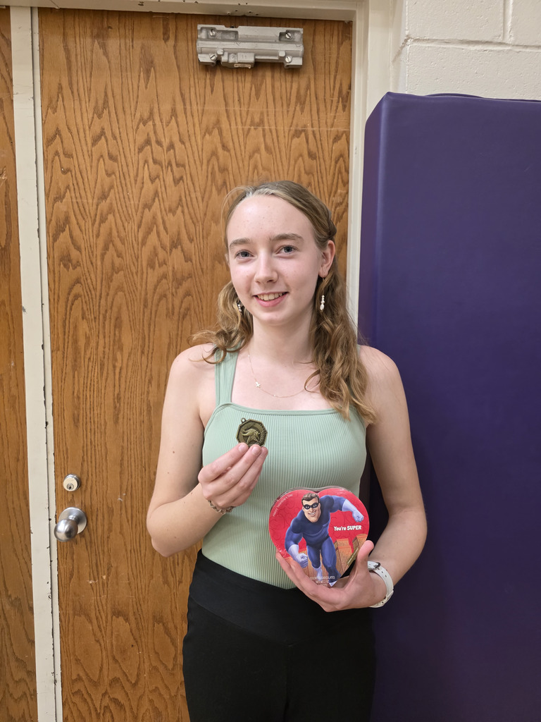 A smiling girl holding up a first place medal and a box of chocolates