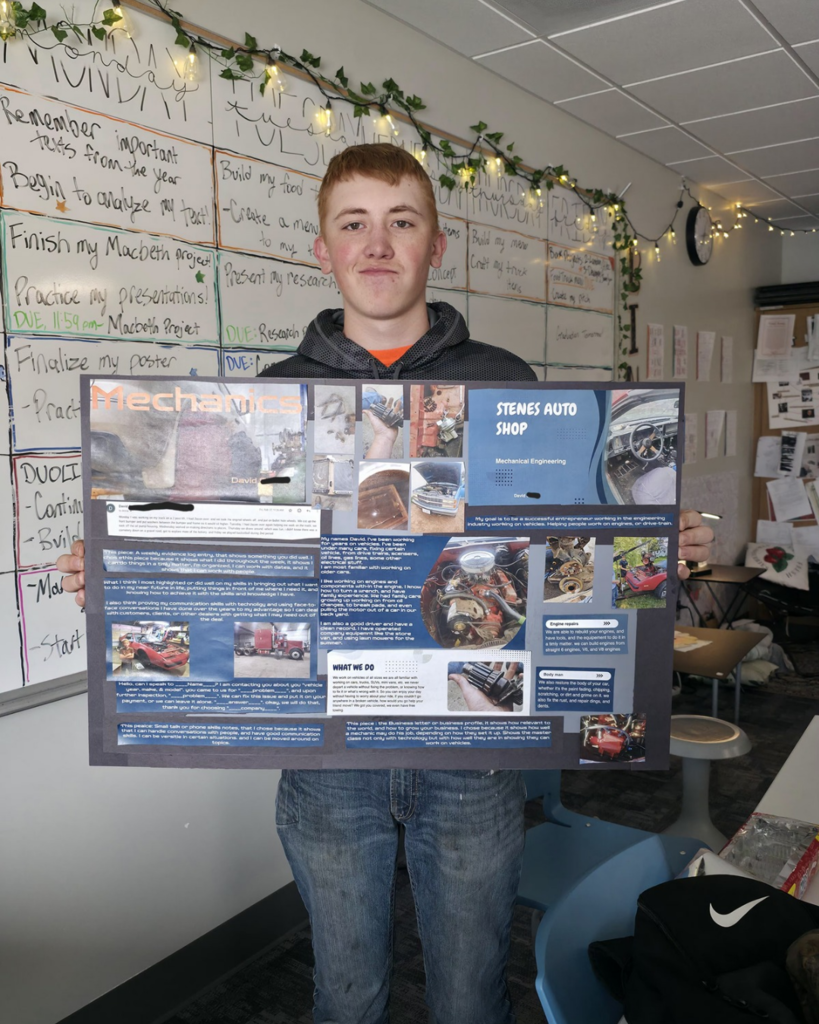 A senior in high school holding a self-made poster about owning his own auto shop.