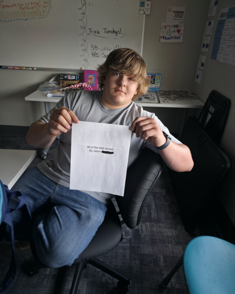 A senior in high school holds up a collection of his stories he wrote titled "All of the best stories"