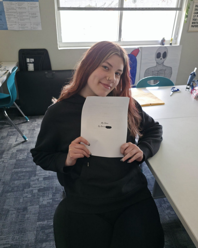 A senior in high school holds up her personal collection of stories and poems she wrote titled "My Ideas"