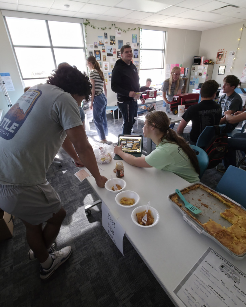 One girl wearing a light green shirt sharing a presentation to a boy wearing gray at a table. There is also butter cake on the table too.