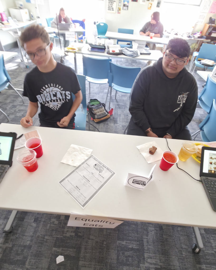 Two boys in black shirts share their food truck called "Equality Eats" in a bright classroom