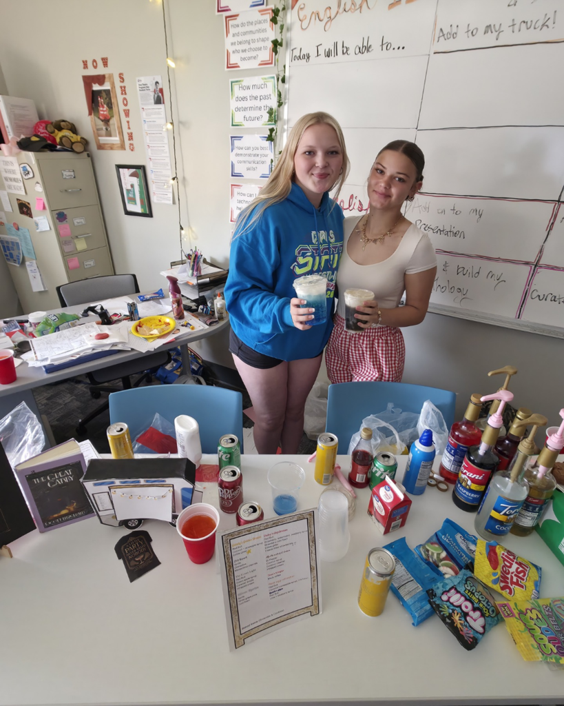 Two girls pose behind their elaborate food truck set up called "The Golden Glass". They also brought a lot of syrups and beverages to make people's orders for the trucks on the spot!
