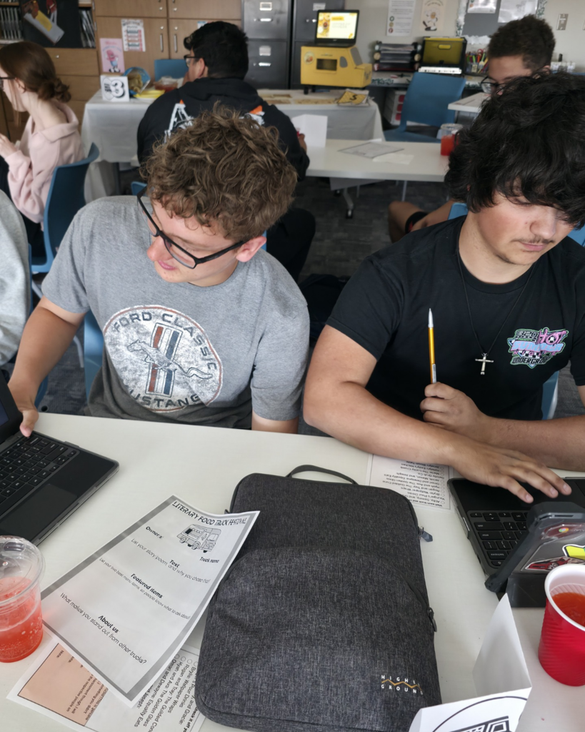 Two boys explain their food truck at a table; their truck is inspired by The Great Gatsby and is called "The Gilded Cone"