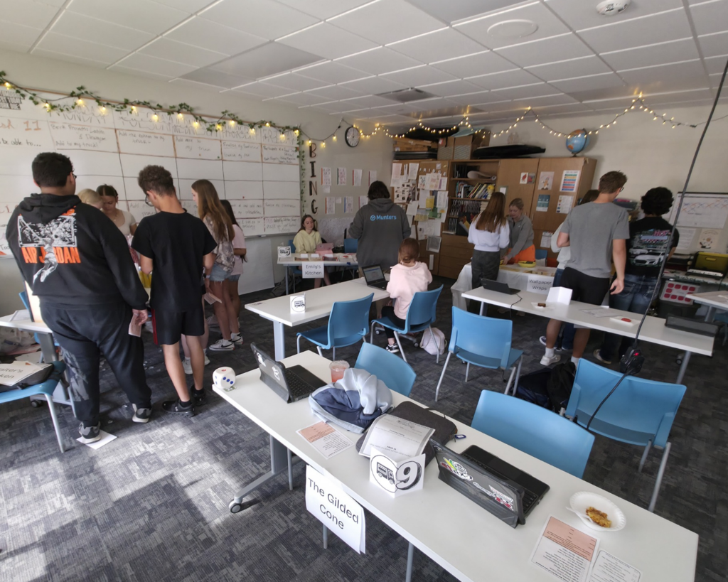 Several students presenting their ideas in a round group setting in a classroom. Other students are listening to their presentations.