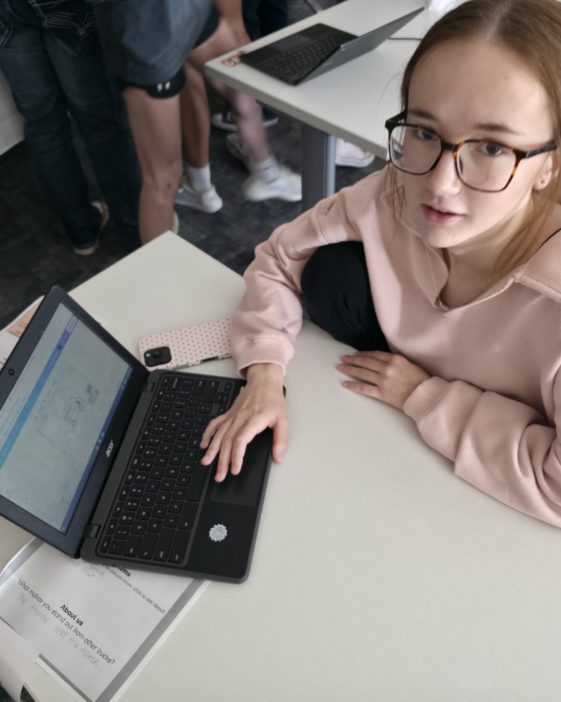 A girl in pink with glasses shows her digital design of a food truck called "Bloom Table"