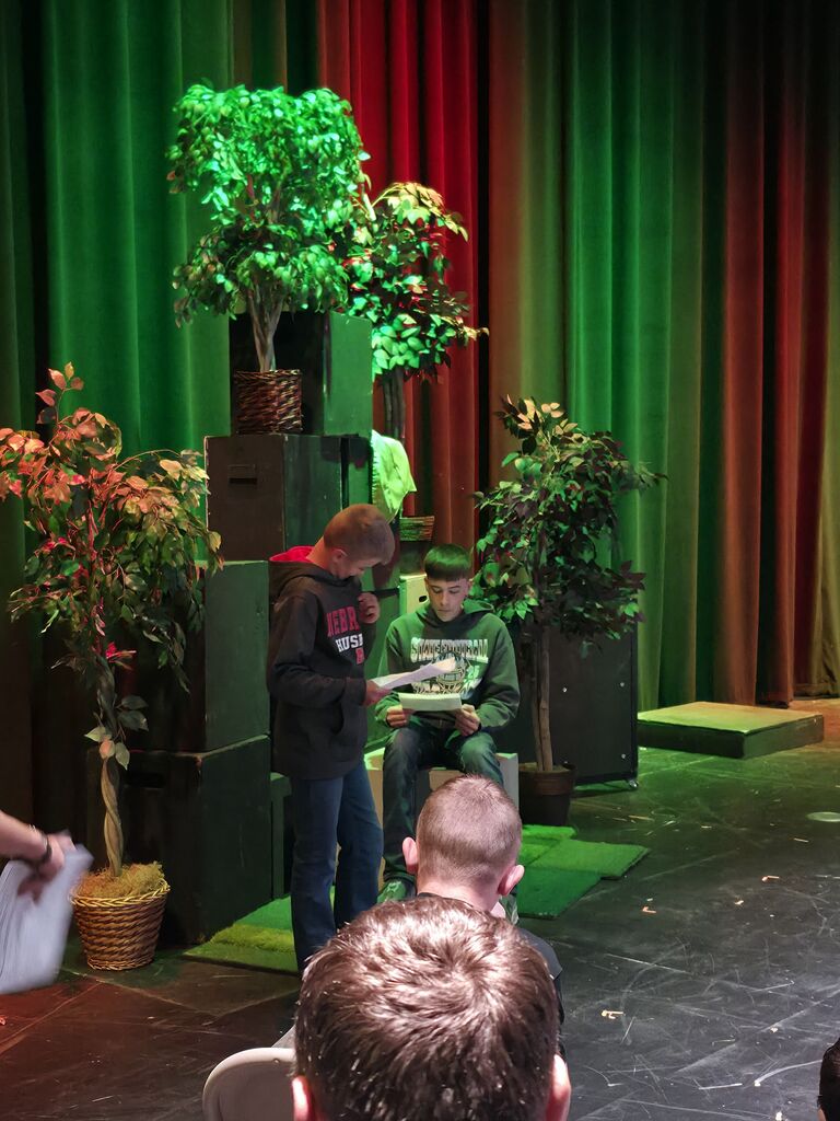 Two boys read scripts in a performance on a stage.