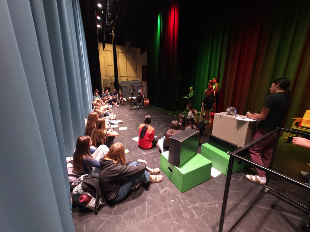 Several students sit and watch a short oerformance on a stage.