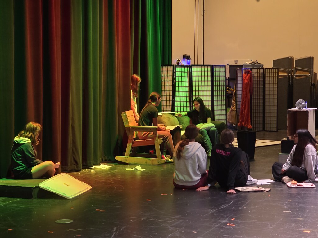 3 girls perform a scene in front of an audience.