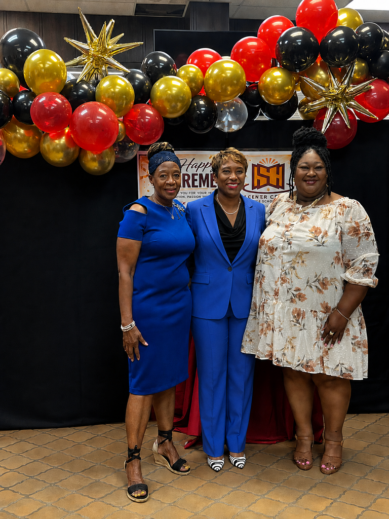 A retirement celebration photo featuring two women standing together in front of a black backdrop decorated with red, gold, and black balloons and gold star accents. One woman is wearing a cream floral dress with tan heels, and the other is wearing a red cardigan with black pants and white shoes. Behind them is a retirement-themed sign for Sumter County Public Schools, creating a festive and celebratory atmosphere.