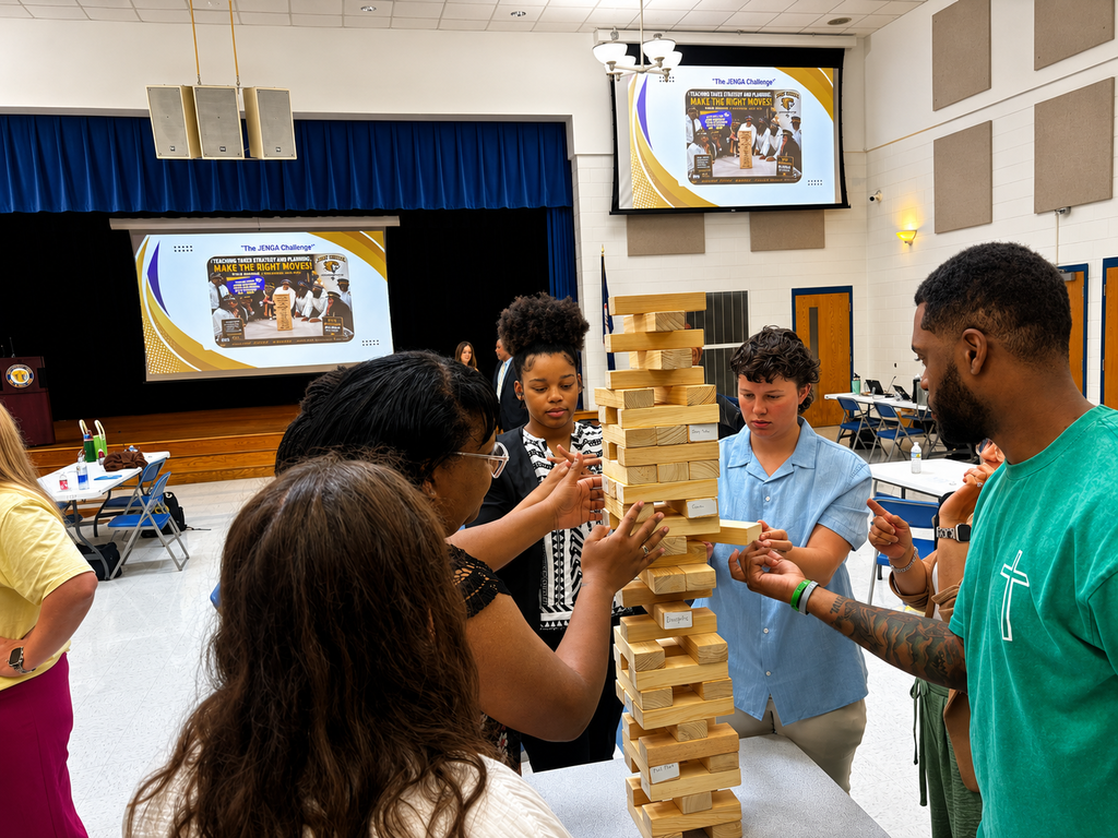 Surry County Public Schools staff participate in a team-building Jenga activity during New Employee Orientation, working together around a large wooden block tower in the school auditorium.