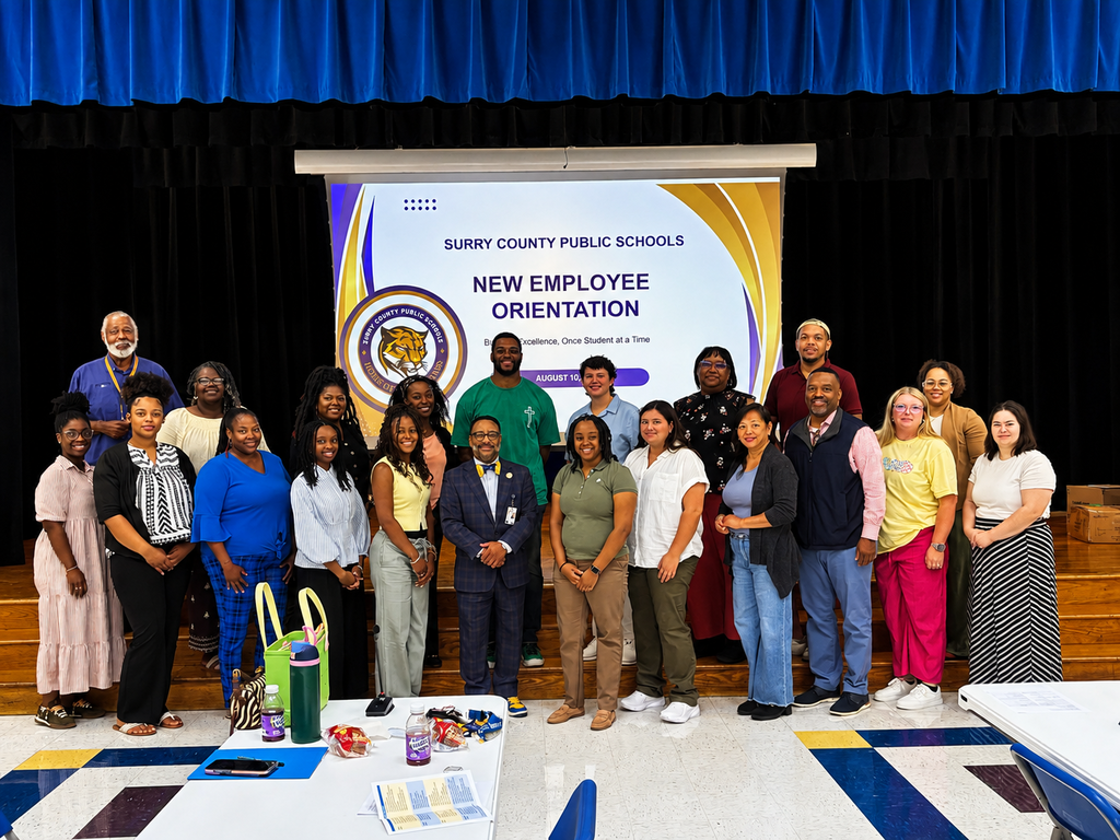 Surry County Public Schools staff and new employees pose together during New Employee Orientation in front of a presentation screen displaying the district logo and orientation welcome slide.