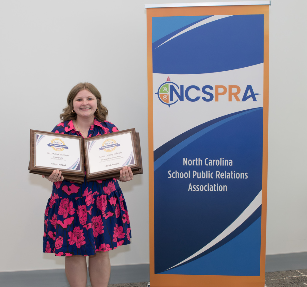 Hollie Lyons-Hawks stands by NCSPRA Banner, smiling with awards