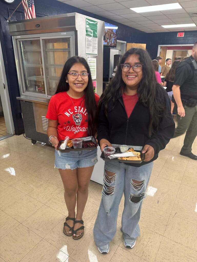 Two girls pose with their lunch plates, smiling