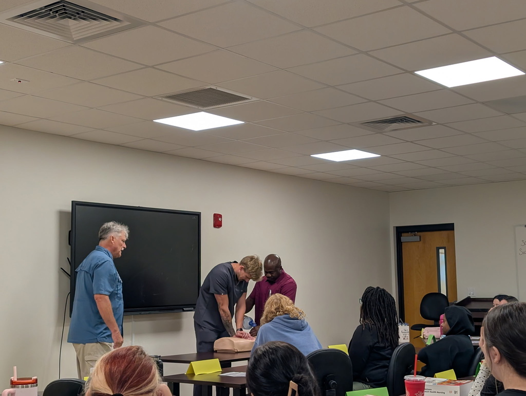Male student performing CPR with fellow classmate while instructor watches 