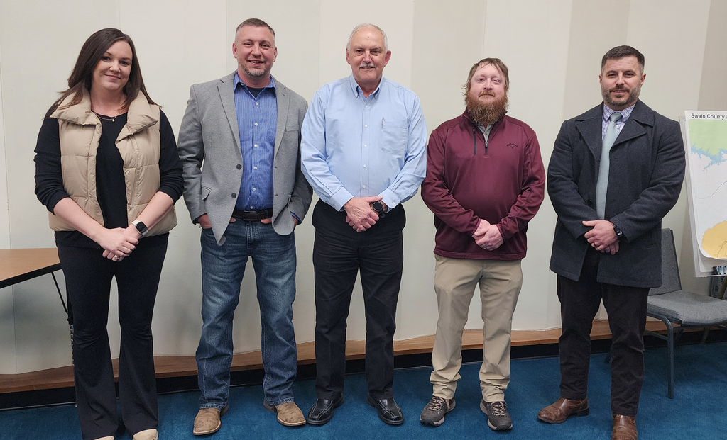 Photo of school board members in a line. One female and then four males in a board room