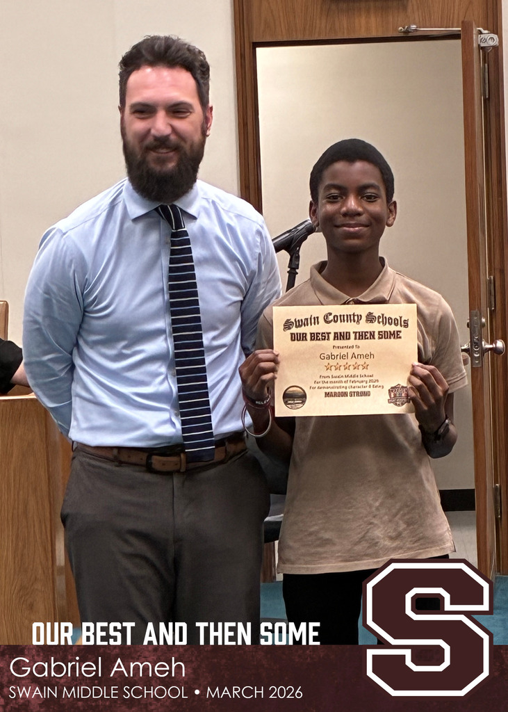 A man in a dress shirt and tie stands next to a young boy holding a Swain County Schools certificate. The boy smiles at the camera as they pose indoors near a doorway.