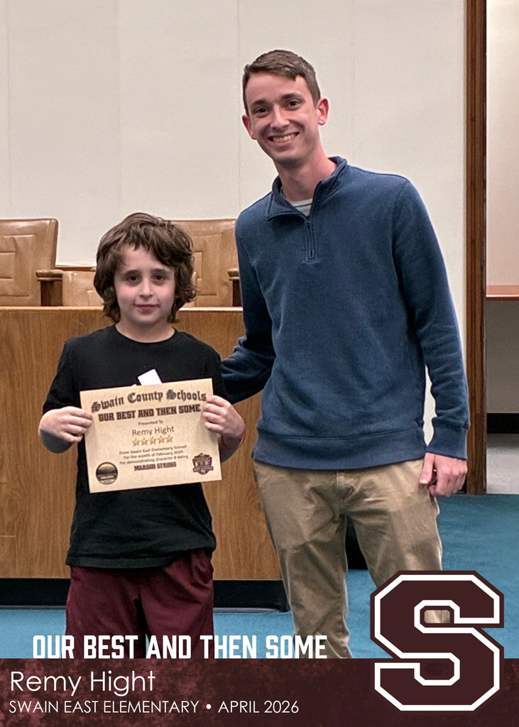 A young boy holds a Swain County Schools certificate while standing next to a smiling man in a blue pullover.