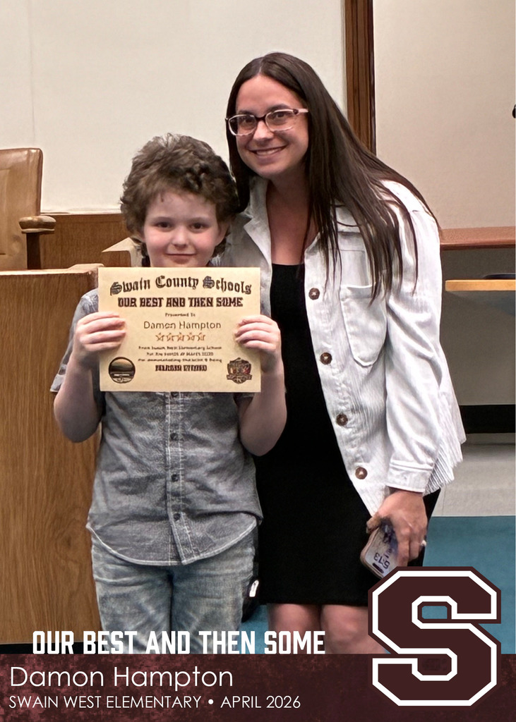 A young boy holds a Swain County Schools certificate while standing next to a smiling woman wearing glasses and a light jacket.