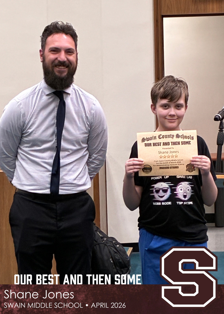 A man in a dress shirt and tie stands next to a young boy holding a Swain County Schools certificate, both smiling in a meeting room.