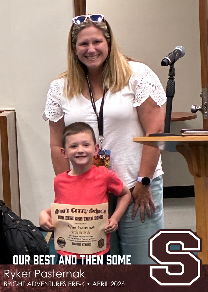 A young boy in a red shirt holds a Swain County Schools certificate while standing in front of a smiling woman in a white blouse.
