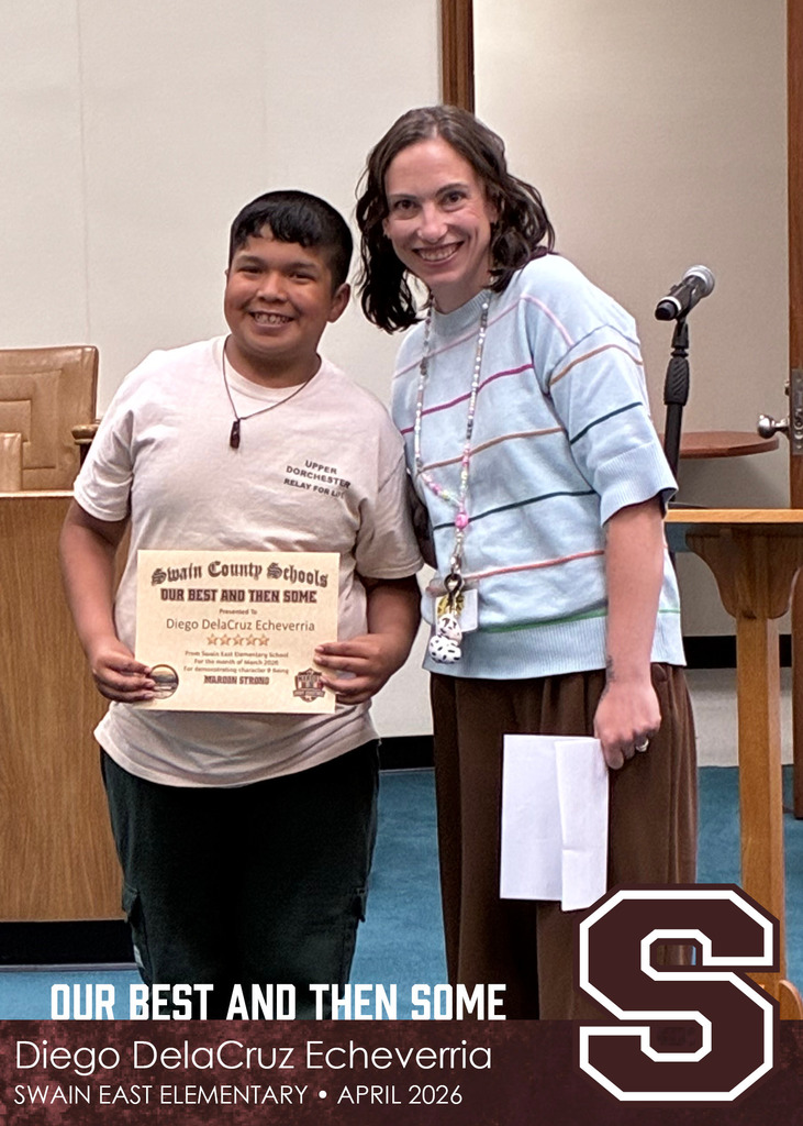 A young boy holds a Swain County Schools certificate while standing beside a smiling woman wearing a striped sweater and lanyard.