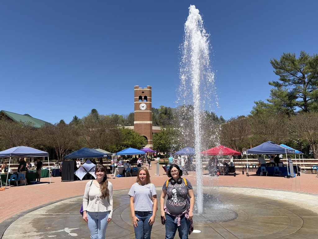Three female students stand in front of a fountain at WCU campus