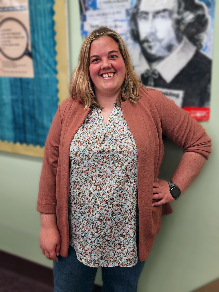 Young woman posing in front of a green wall with a poster of William Shakespeare .