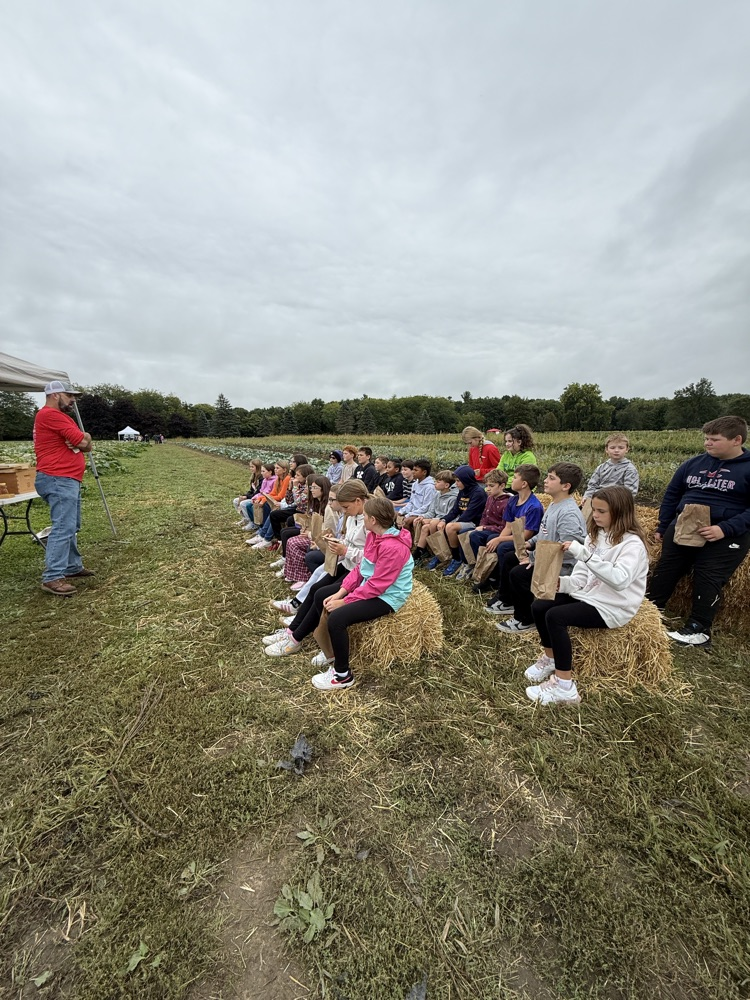 Fourth graders sitting on hale bales listening to a farm presentation at Schomaker Farms.