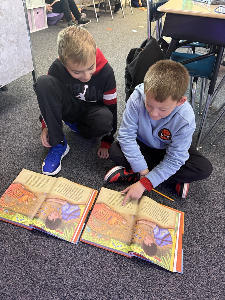 Two boys reading the same story together on the carpet.