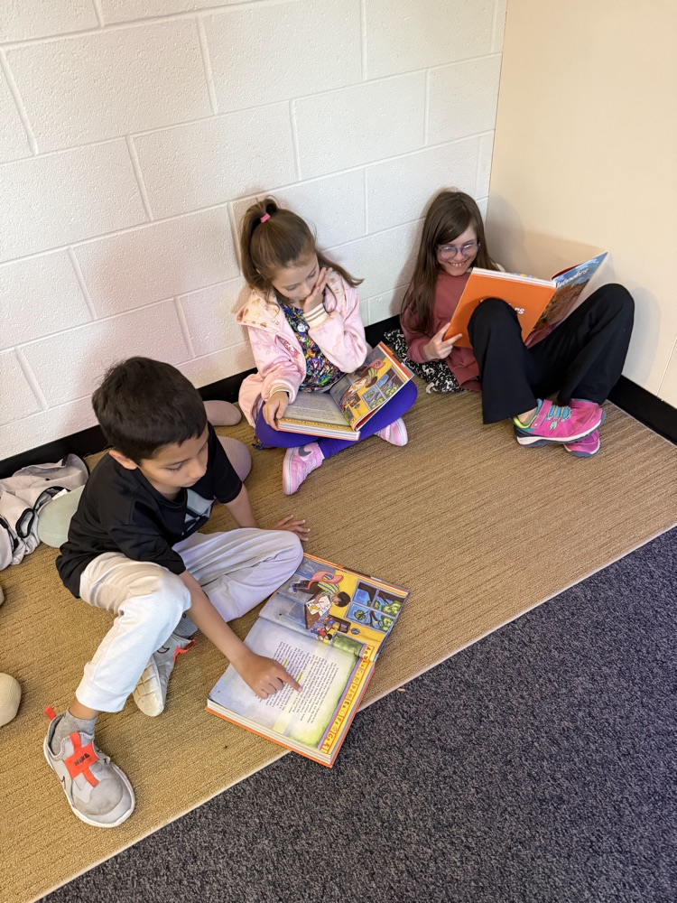 Three students reading the same story together while sitting on the floor.