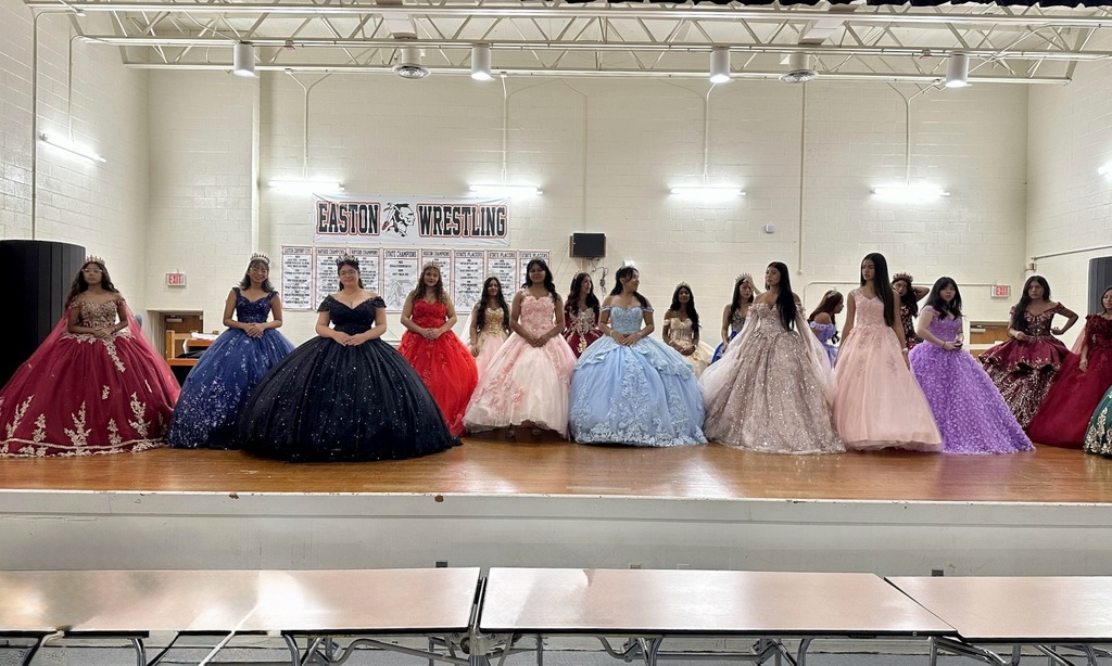 Hispanci female students in colorful formal gowns on the stage in the Easton High cafeteria.