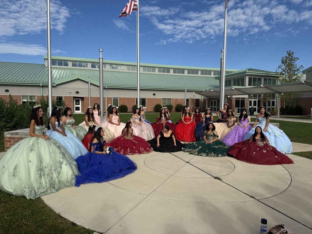 Hispanic female high school students in colorful formal gowns in front of Easton Elementary School.