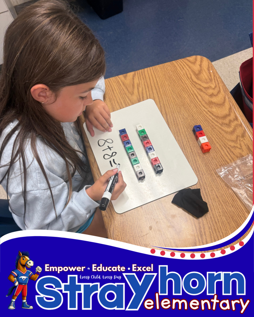 student with cubes and marker writing addition facts on whiteboard at desk
