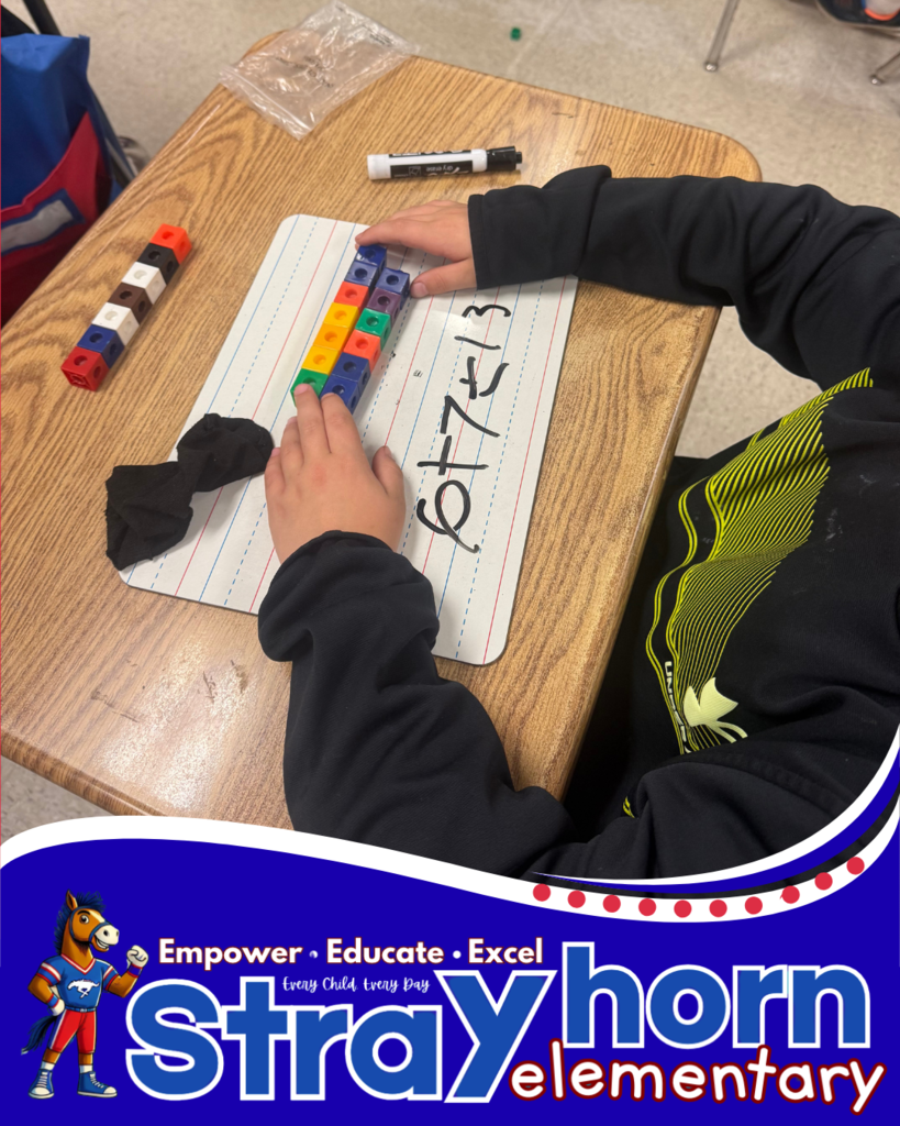 student with cubes and marker writing addition facts on whiteboard at desk