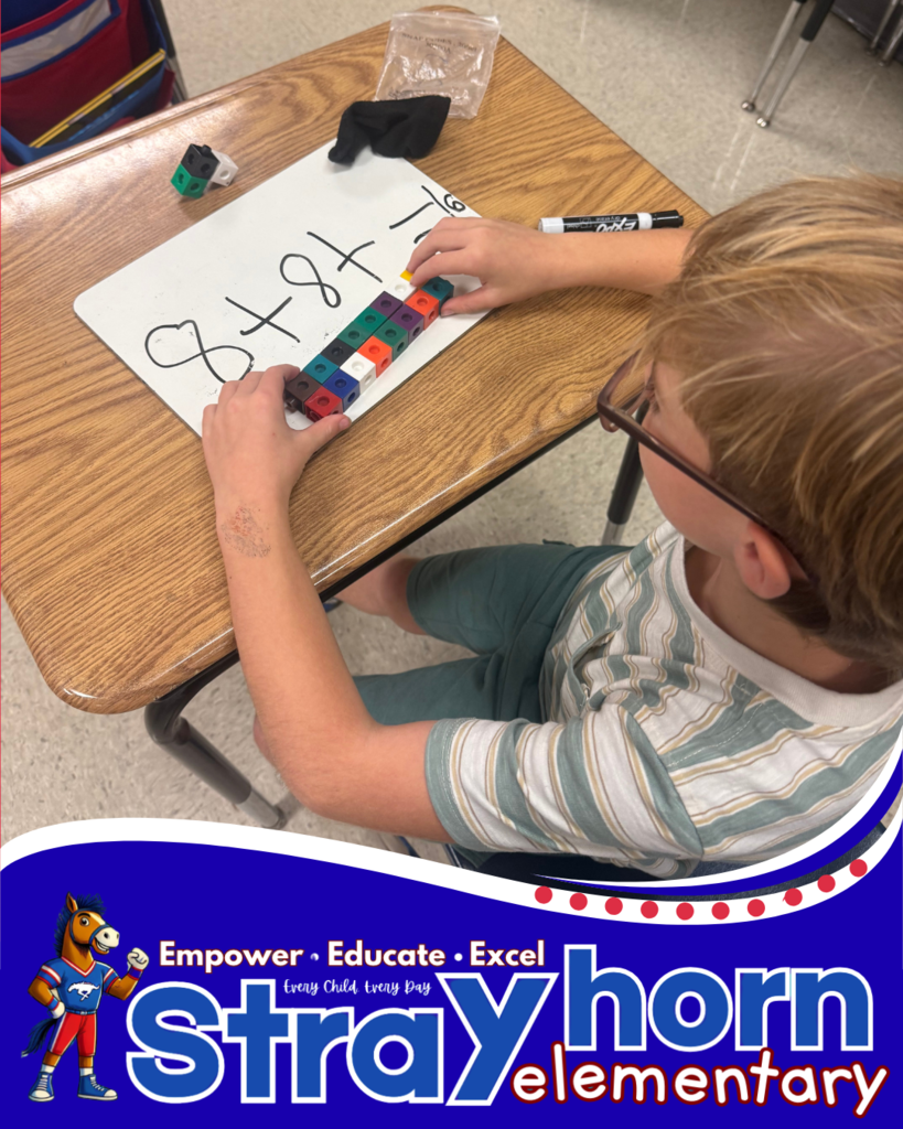student with cubes and marker writing addition facts on whiteboard at desk