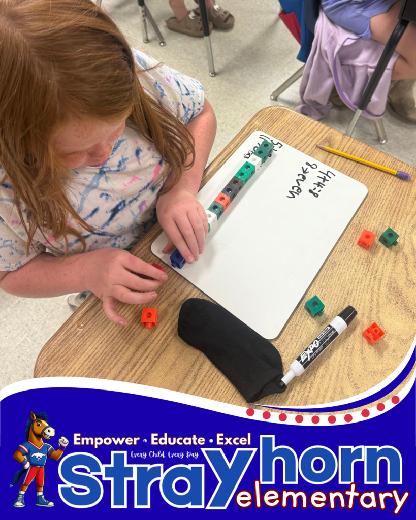 student with cubes and marker writing addition facts on whiteboard at desk