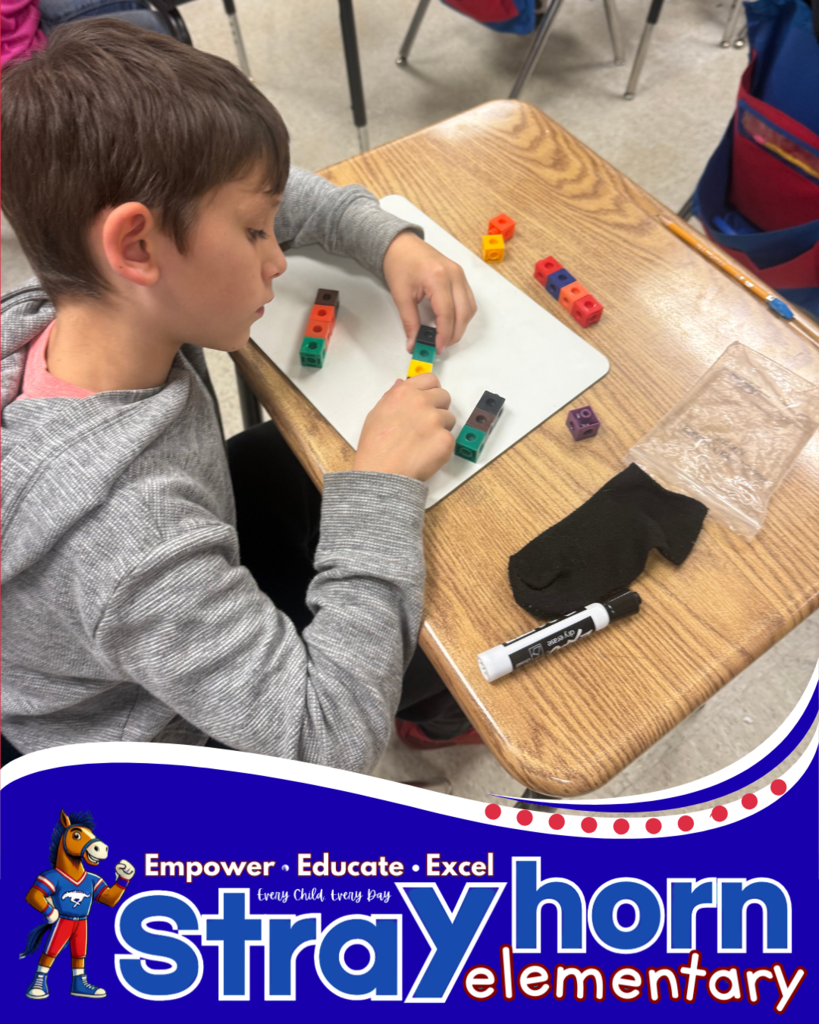 student with cubes and marker writing addition facts on whiteboard at desk