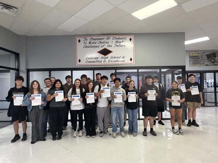 A group of students stand in a hallway holding certificates, with a banner behind them reading "N. Rind".