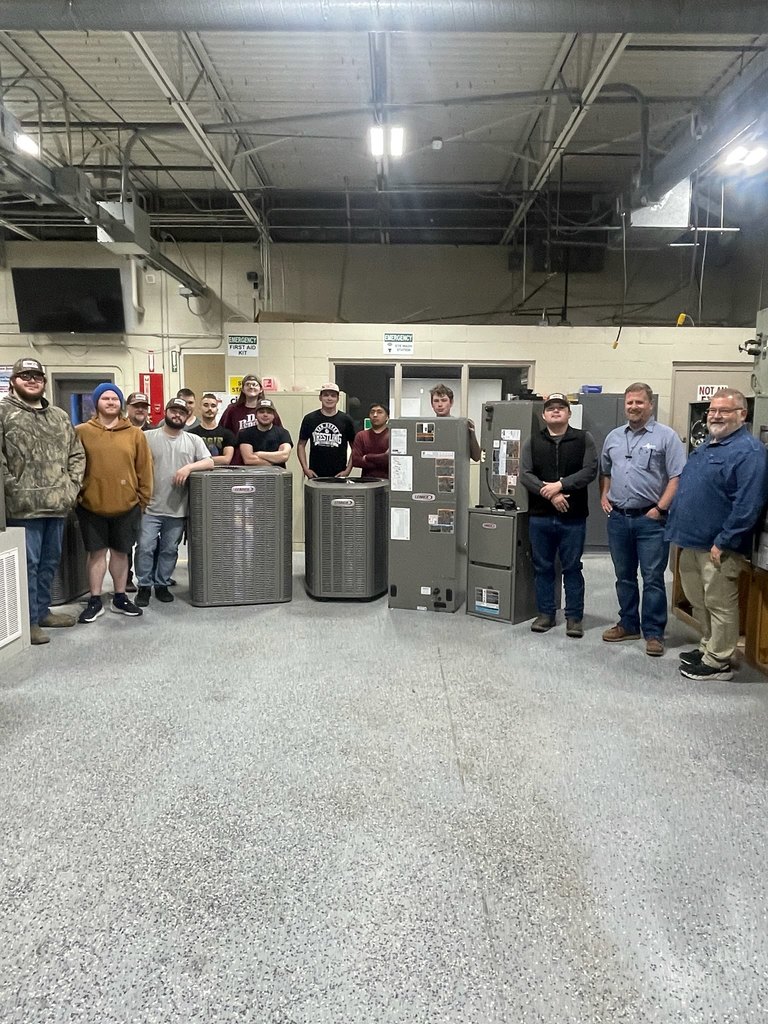 A group of people in winter wear stand in a warehouse. They are surrounded by large gray appliances.