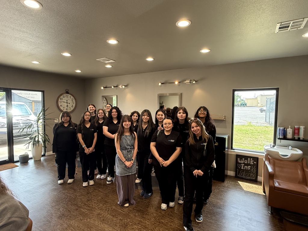 A group of women in black clothing stands in a room with wood floors, a clock, and windows.